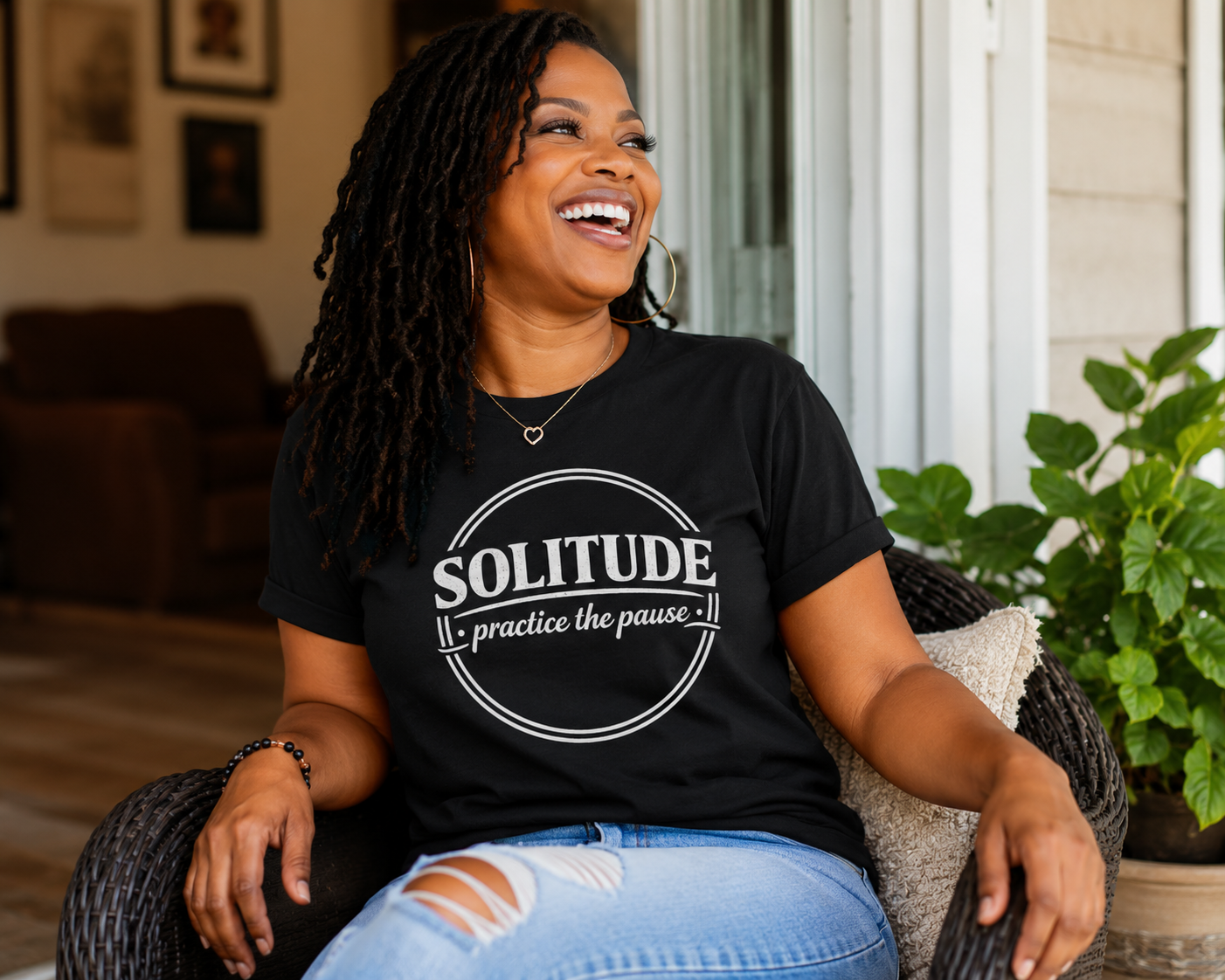 Woman wearing a black t-shirt with 'Solitude: practice the pause' text, sitting outdoors.